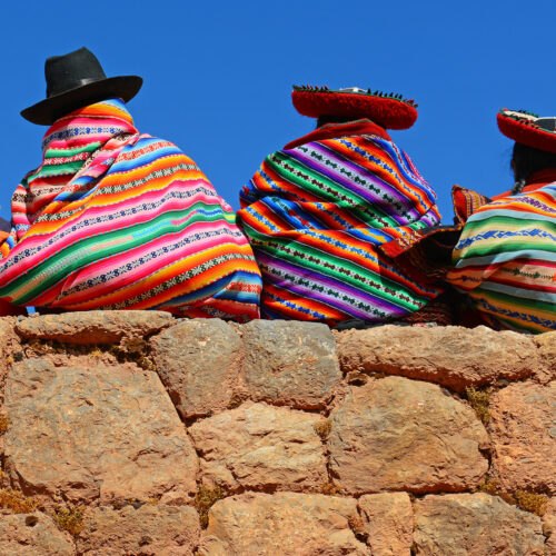 Chincheros, Peru - June 23, 2013: Quechua ladies with colorful textiles and hats sitting on an ancient Inca Wall together with a young boy with modern clothing.
