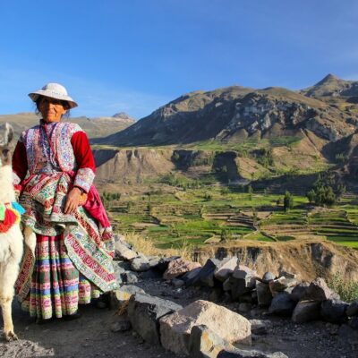 Colca, Peru - January 16, 2015: Local woman with llama standing at Colca Canyon in Peru. It is one of the deepest canyons in the world with a depth of 3,270 meters.