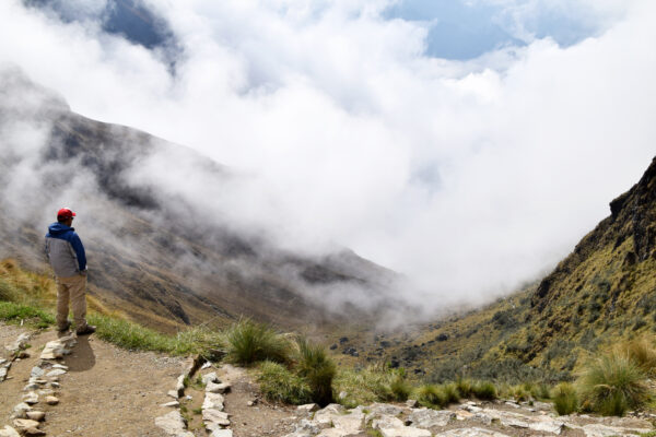 Hispanic man at the mountain pass known as Dead Woman's Pass, on the historical Inca trail, which goes through the mountains to Machu Picchu. Man at over 4000 m high altitude, seeing the clouds coming in covering the mountains. Photo taken on the Inca trail, Peru on November 3, 2018