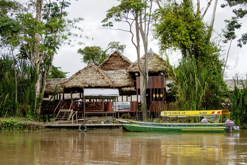 A thatched river lodge on the water in the Peruvian Amazon, with a boat moored alongside
